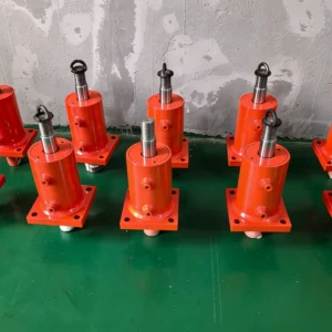 Multiple orange tie-rod cylinders with mounting bases on green surface.